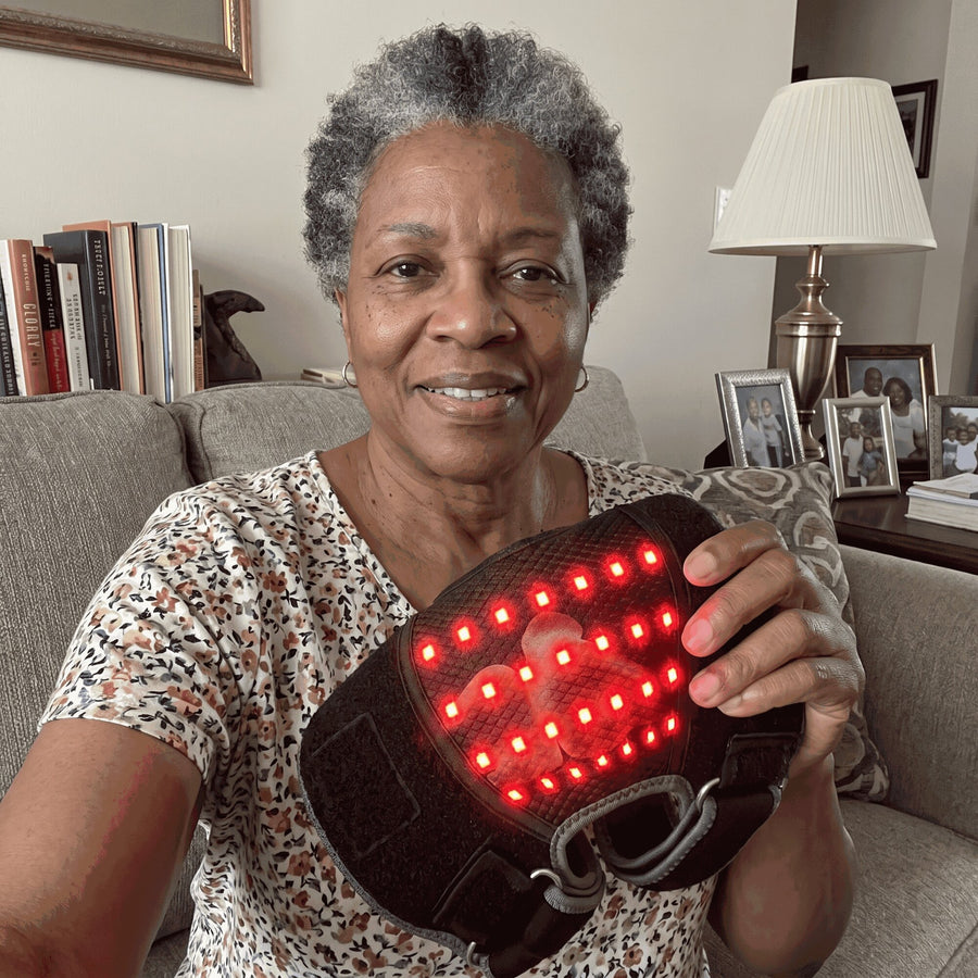 Smiling woman on her sofa holding the Bellrose Warmth Massager with its red lights on