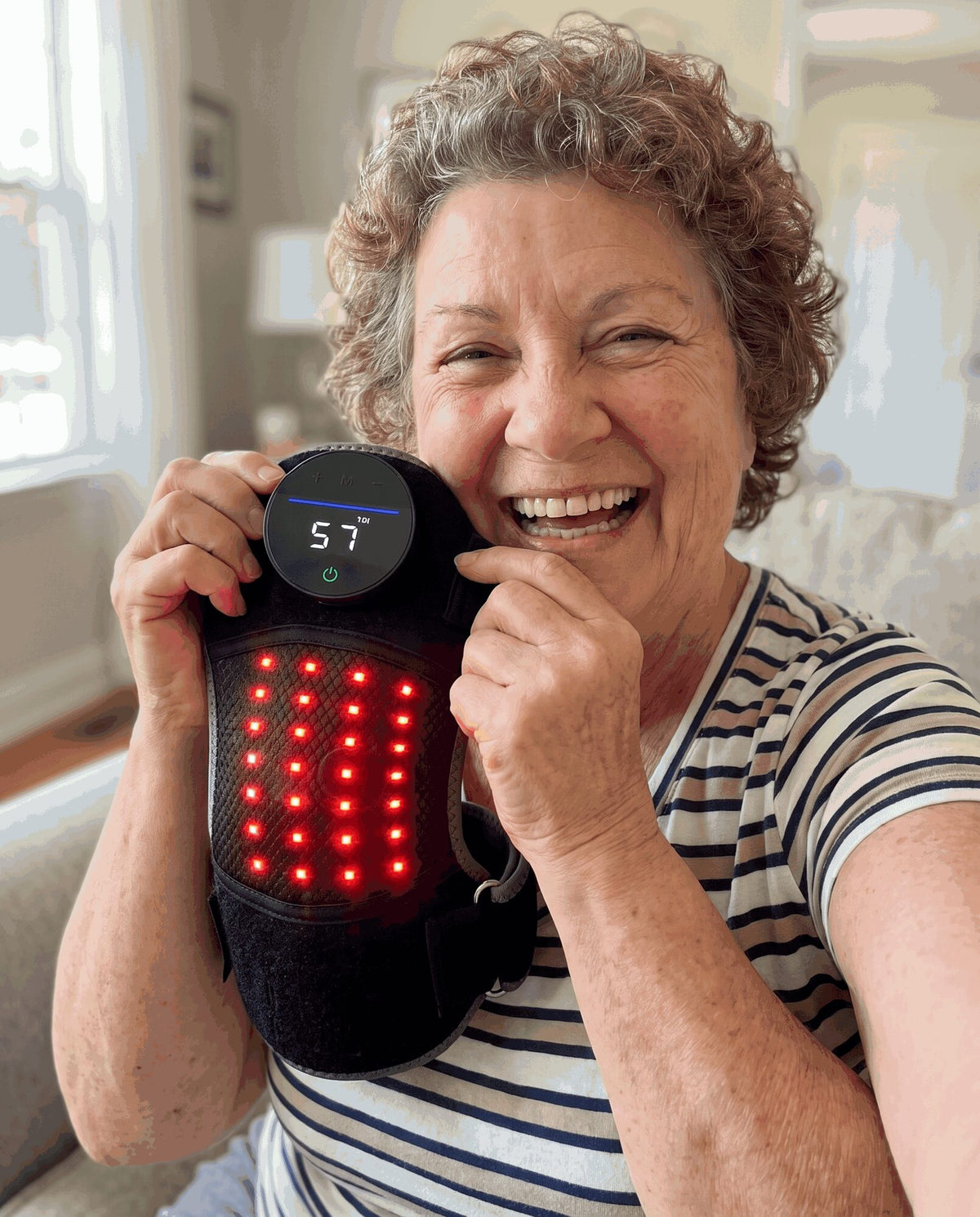 Laughing woman with curly gray hair in a striped shirt holding the Bellrose knee wrap up beside her face